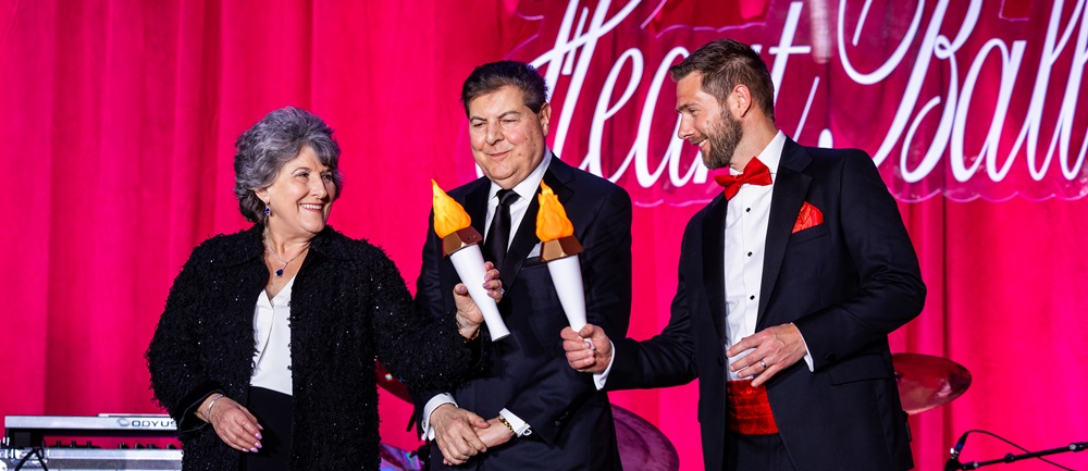 Three people on stage in front of Heart Ball sign holding torches.